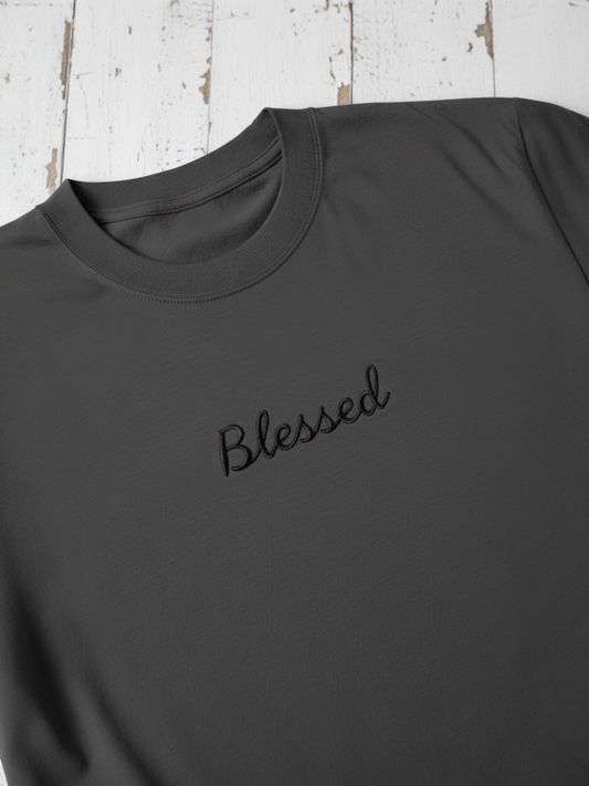 Dark gray sweatshirt with 'Blessed' embroidery on a wooden surface