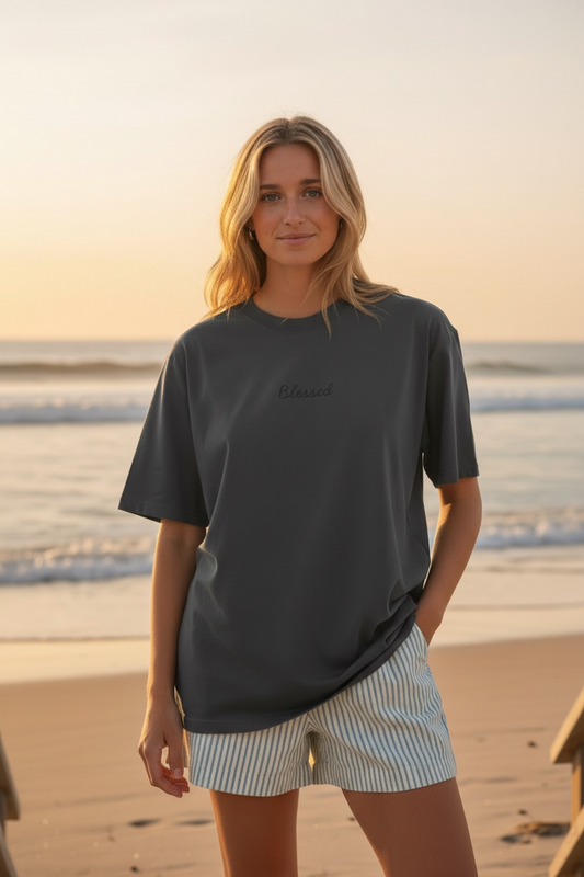 Woman wearing a dark gray t-shirt and light shorts standing on a beach at sunset.