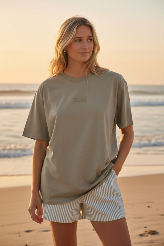Woman standing on a beach wearing a beige t-shirt and striped shorts.