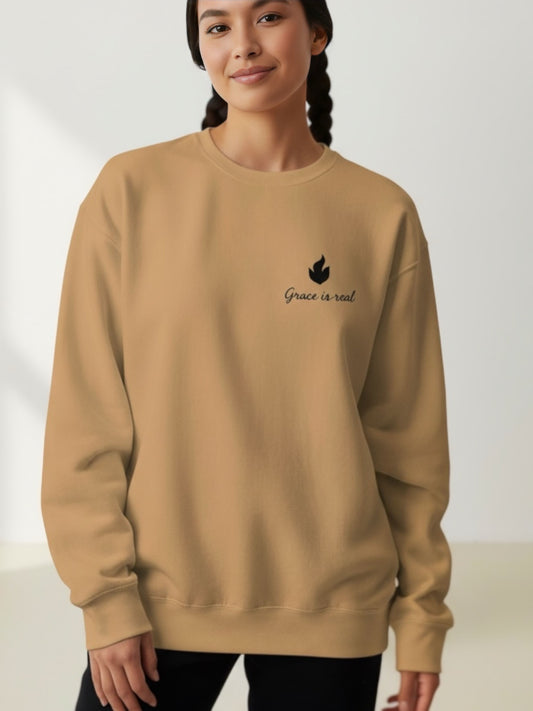 Person wearing a beige sweatshirt with text and a leaf design on a plain background