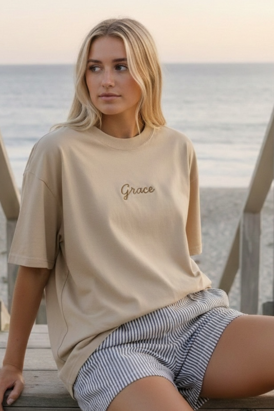 Woman wearing a beige t-shirt with 'Grace' on it at the beach.