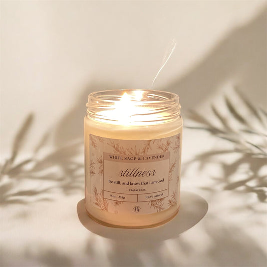 Stillness Candle – White Sage & Lavender glowing softly with leaf shadows, calming soy candle by Holy Grace.