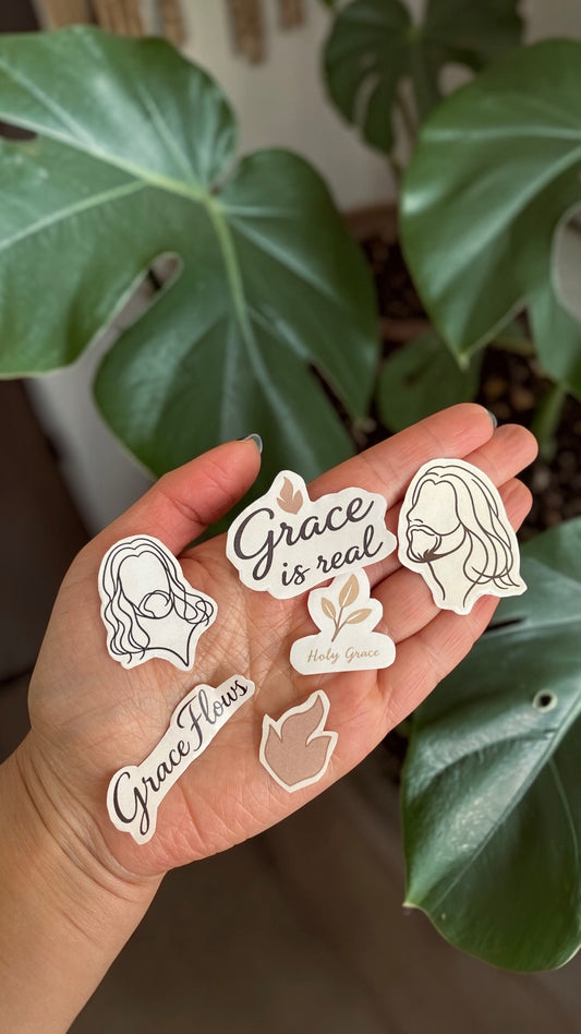 Hand holding stickers with motivational phrases and designs against a green leafy background