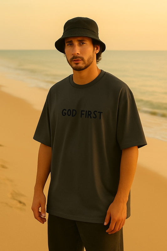 Man standing on the beach wearing God First oversized black tee — Holy Grace