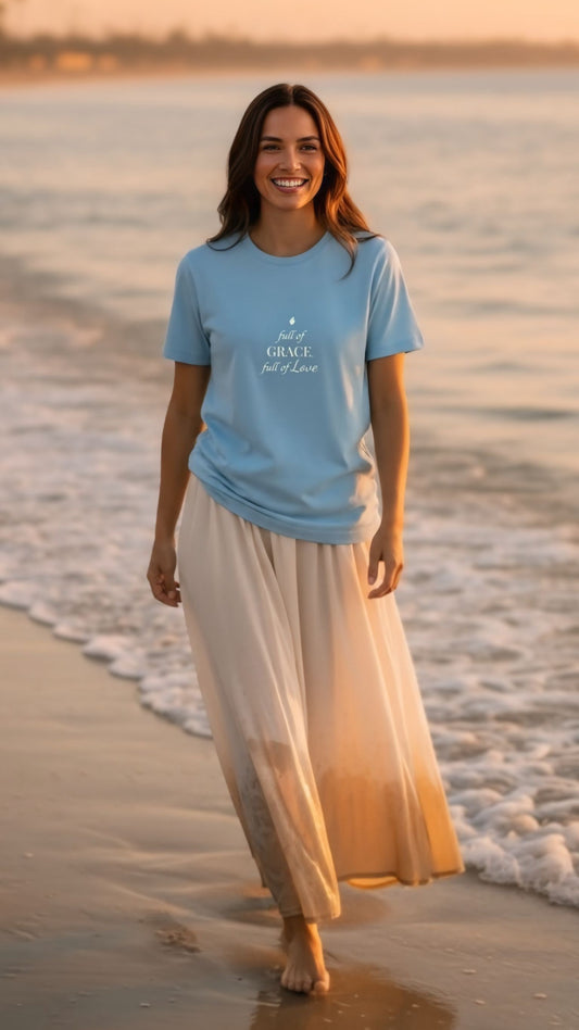 Woman wearing a blue t-shirt with text on it, standing on a beach.