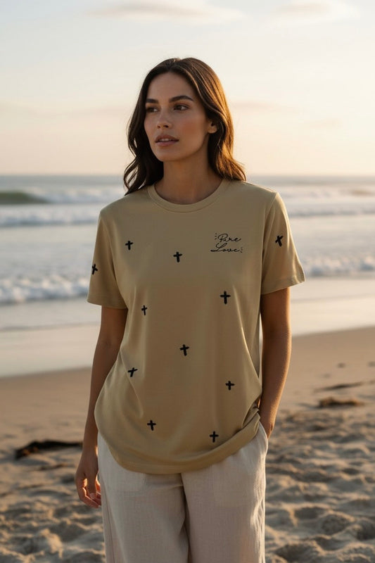 Woman wearing the beige Pure Love unisex cross tee on the beach at sunset, front view.