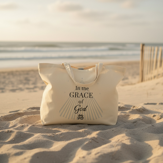 Beige tote bag with 'In the Grace of God' text on a sandy beach